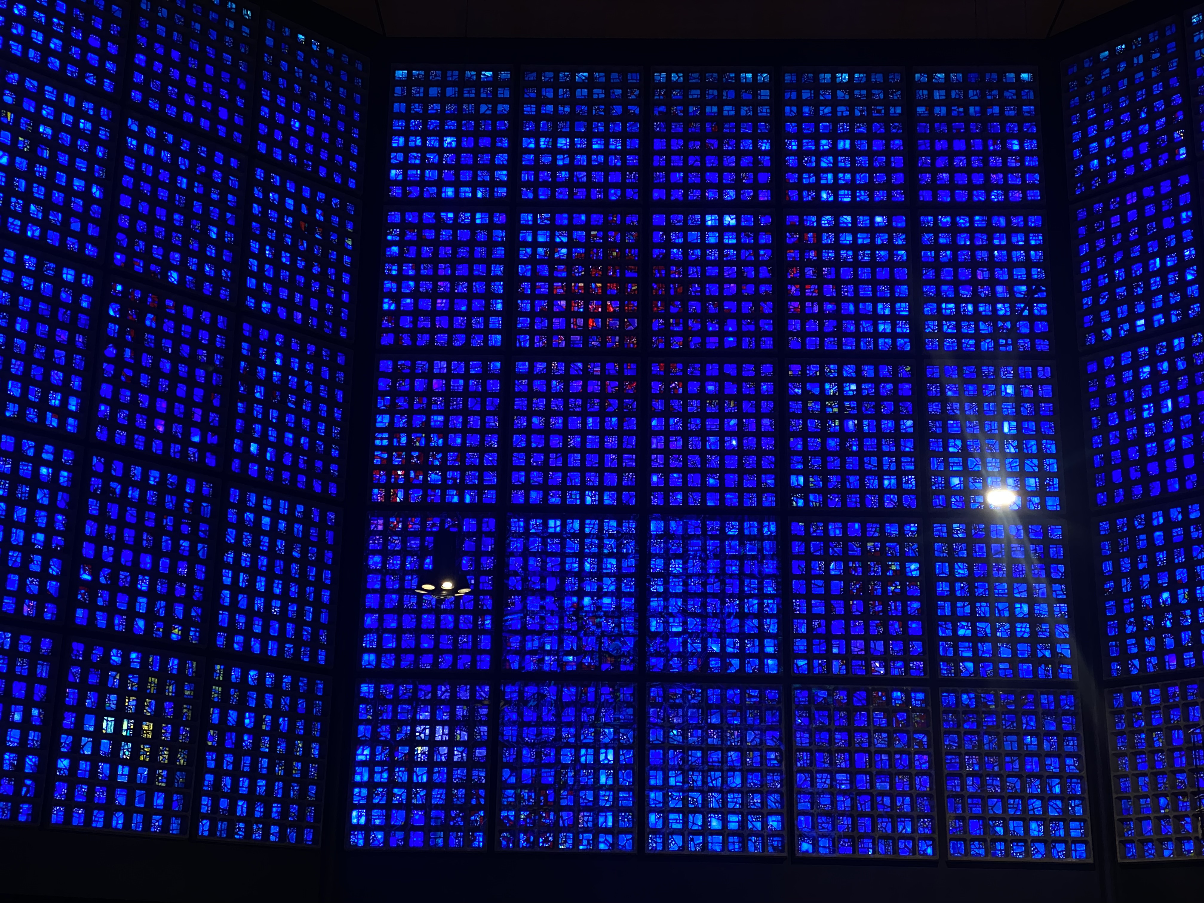 A wall of deep, electric blue glass blocks filling the frame — transcendent blue light flooding an interior space